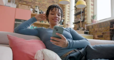 African American Student on Couch looking at Smartphone in Loft apartment Stock Footage 297256996