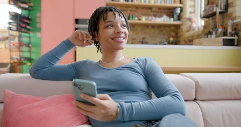 African American Student on Couch looking at Smartphone in Loft apartment Stock Footage 297258284
