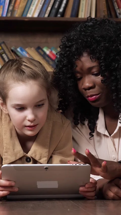 African american teacher explaining a lesson on a digital tablet to a young Stock Footage 341445096