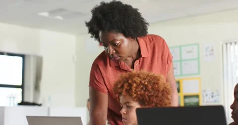 African American teacher in rust top leaning at desk, teen student asking help, Stock Footage 335747226