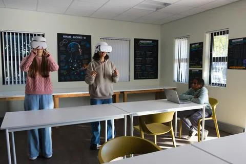 African American teens using VR headsets gesturing in classroom while peer Stock-Fotos