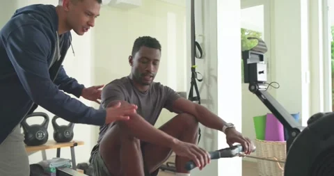 African American trainee rowing on rowing machine under trainer guidance, Stock Footage 340611357