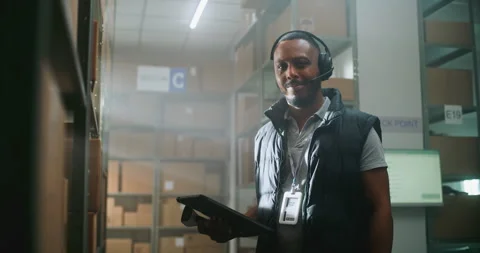 African American Warehouse Associate Talks with Client, Uses Tablet, Looks at Video stock 307716216