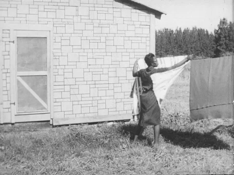 African-American woman hangs bedsheets on a clothesline to air them out. Stock Footage