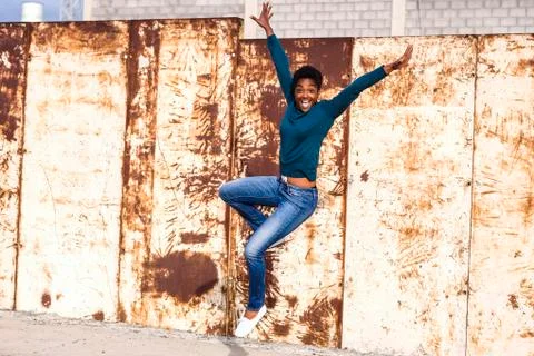 African American woman jumping for joy near rusty metal wall Stock Photos