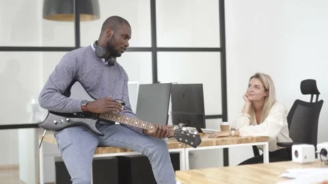 African-American worker taking a break and playing electric guitar in the office Stock Footage 233756431