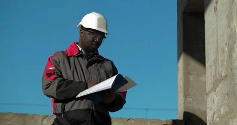 African american workman at construction site, looks in work papers Stock Footage 203965701