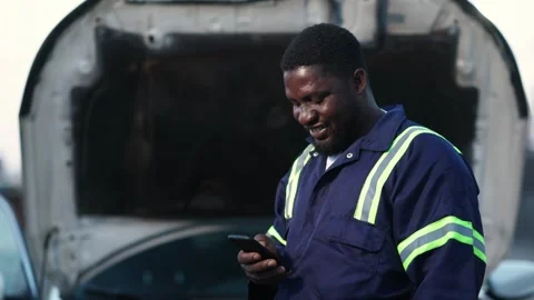 African auto mechanic uses smartphone for business in workshop, SME owner Stock Footage 346641561