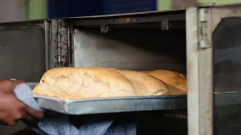 African baker removes fresh hot bread loaves from oven, SME entrepreneur Stock-Footage 346565520