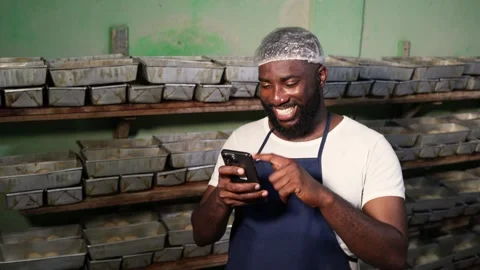 African baker uses smartphone for online orders and digital banking in bakery Stock Footage 346565352
