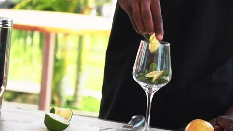 African bartender putting lime in a cocktail glass, making passion fruit mojito Stock Footage 230080309