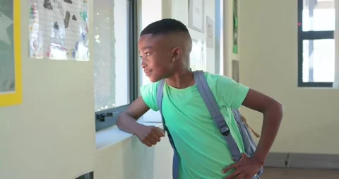 African boy leaning at school window, glancing outside, turning to camera with Stock Footage 340987058