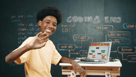 African boy use laptop to code program and turn around to wave hand. Edification Photos