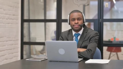 African Businessman with Headset Looking at Camera while Working on Laptop Video stock 301308019
