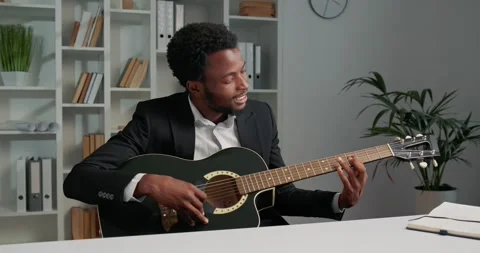 African businessman playing guitar while sitting at the office, looking happy. Stock Footage 253825508