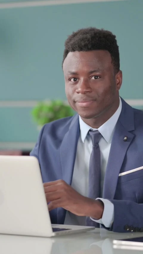 African Businessman Smiling at Camera while using Laptop in Office, Vertical 스톡 동영상 339574450
