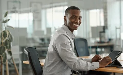 African businessman smiling while using a tablet at a desk Stock Photos