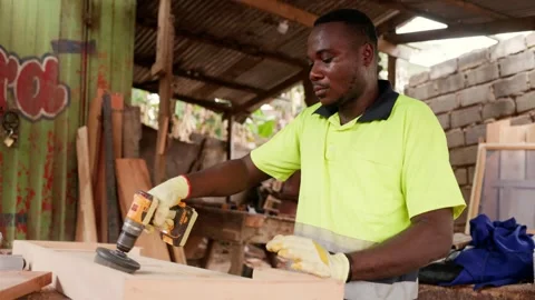 African carpenter using hand drill with brush attachment on wooden door  Stock Footage 346733862