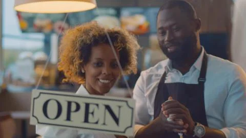 African cheerful small business owners smiling and turning open sign on cafe Stock Photos