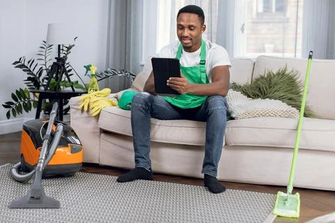 African cleaner using digital tablet while relaxing on couch Stock Photos