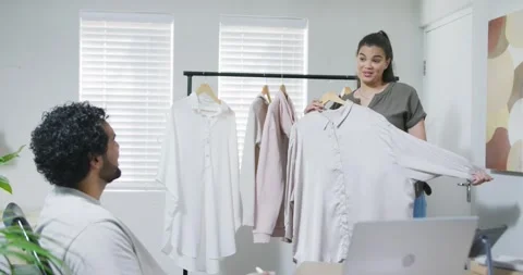 African colleagues presenting light button blouse by clothing rack per client Stock Footage 344458260