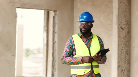 African construction engineer in hard hat and safety vest holding a smart tablet 库存影片 346257590