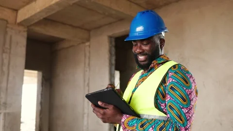 African construction engineer smiles confidently holding tablet on-site Stock Footage 346258213