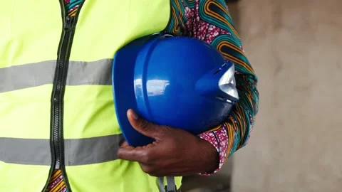 African construction worker in high-vis vest holds blue hard hat on site 库存影片 346258323