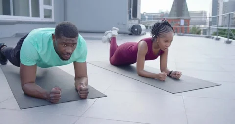 African couple exercising on rooftop, man shifting into forearm plank for core Stock Footage 337943975