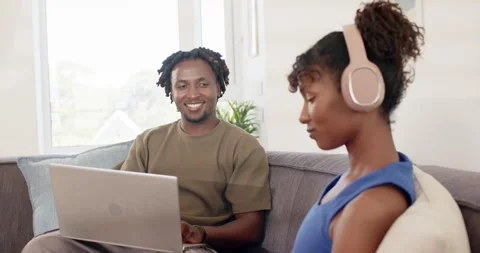 African couple at home, man smiling at laptop, leading woman in pink headset Stock Footage 344535341