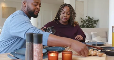 African couple preparing meal at dining table, woman lifting French press, man Stock Footage 339495442