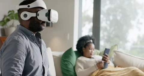 African couple sitting on couch, man with VR headset gesturing after prompt, Stock Footage 338337332