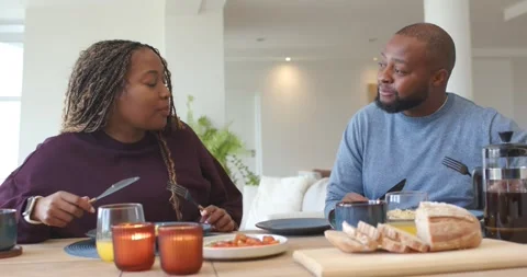 African couple sitting at dining table sharing breakfast, woman turning toward Stock Footage 339495491