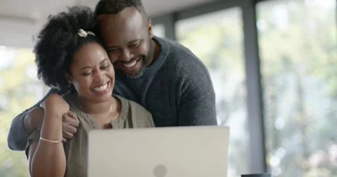 African couple sitting at table man coming leaning over shoulder woman typing Vídeo Stock 342363048