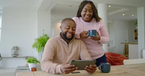 African couple using tablet at dining table woman leaning with mug, man tapping Stock Footage 340674257