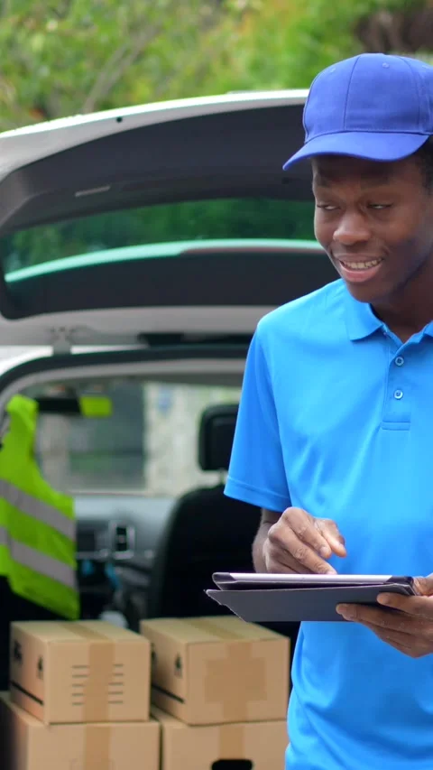 African delivery man using digital tablet standing next to van Stock Footage 284510905