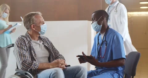 African doctor in safety mask consulting disabled man patient in hospital Stock Footage