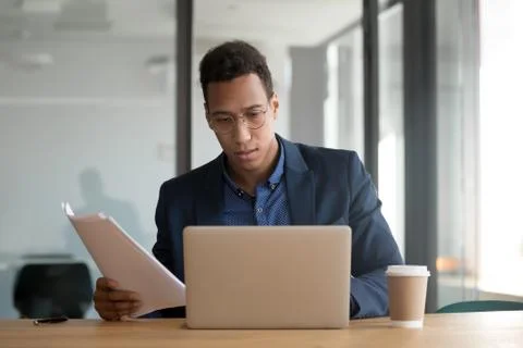 African ethnicity businessman checking documents using laptop working in office Stock Photos