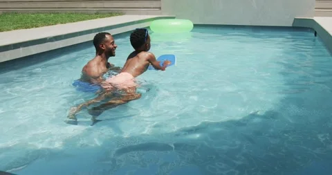 African father and son practicing kicking with blue kickboard in backyard pool Vídeo Stock 342392798