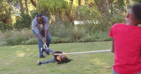 African father pulling long white rope, youth in yellow rolling on lawn, son Stock Footage 336667910