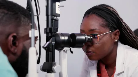 African female optometrist using slit lamp machine for eye exam on patient  Stock Footage 346770951