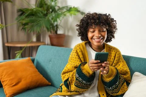 African girl holding smartphone touch screen typing scroll page at home. Woman Stock Photos
