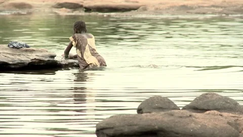 An African girl washes clothes while standing waist-deep in a river. Stock Footage 179864182