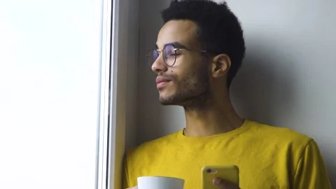 African guy drinking coffee from a mug by the window Stock Footage 166197034