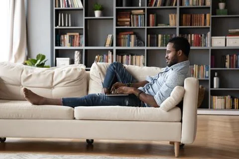 African guy lying on sofa typing message using computer Stockfoto's