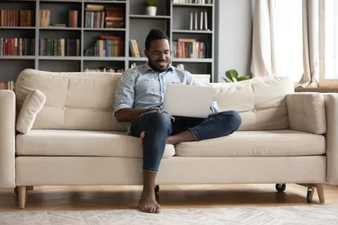 African guy rest on sofa using notebook watching movie Stock Photos
