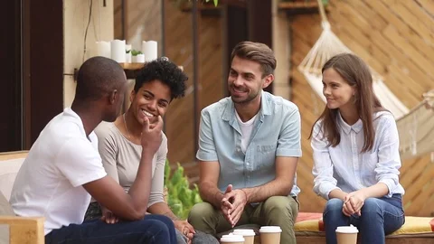 African guy talking to diverse friends sitting on cafe terrace Stock Footage 107843986