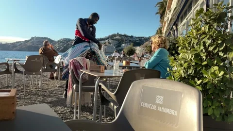 African immigrant trying to sell textiles to woman at café Stock Footage 167977453