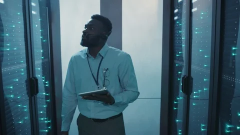 African IT administrator holding tablet walking in server rack corridor Stock Footage 119081897