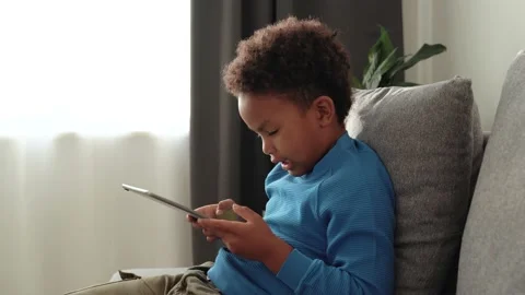 African kid boy sitting on sofa with tablet device, play video game Stock Footage 170033892